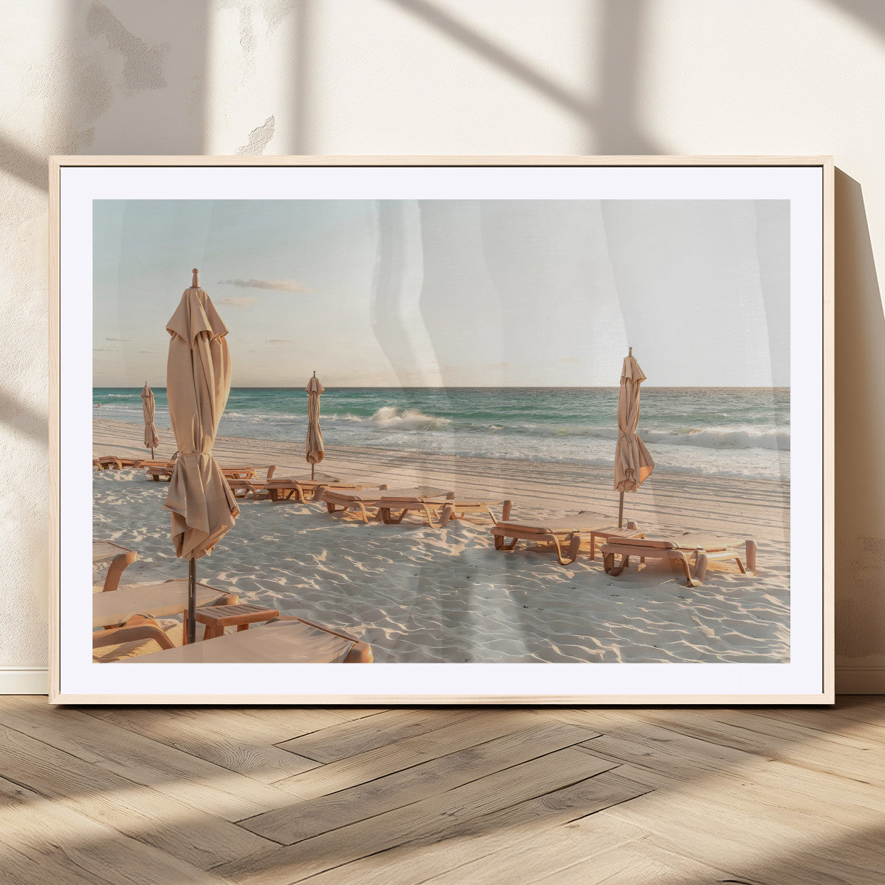 Minimalist photo of empty beach loungers and umbrellas on soft sand, ideal for calm seaside or pastel coastal-style home decor.