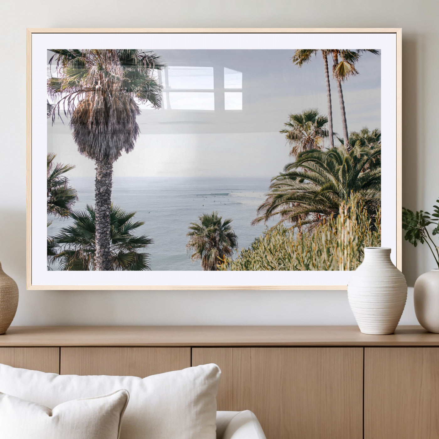 Scenic coastal view with tall palm trees overlooking a calm ocean, soft blue waves, and surfers in the distance, creating a peaceful tropical vibe.