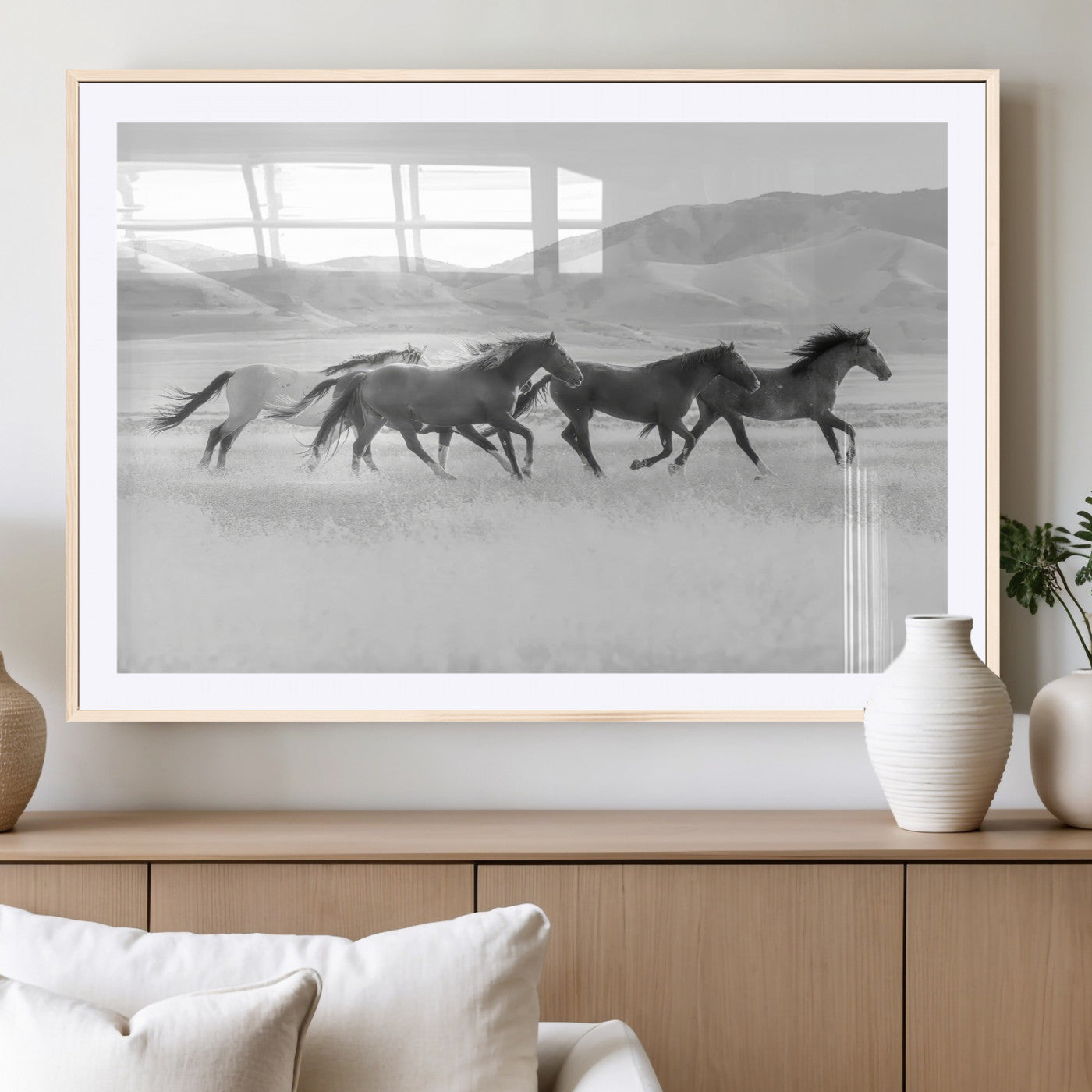 A black and white image of wild horses running freely across an open grassland, capturing the power and beauty of untamed nature in a rustic western setting.