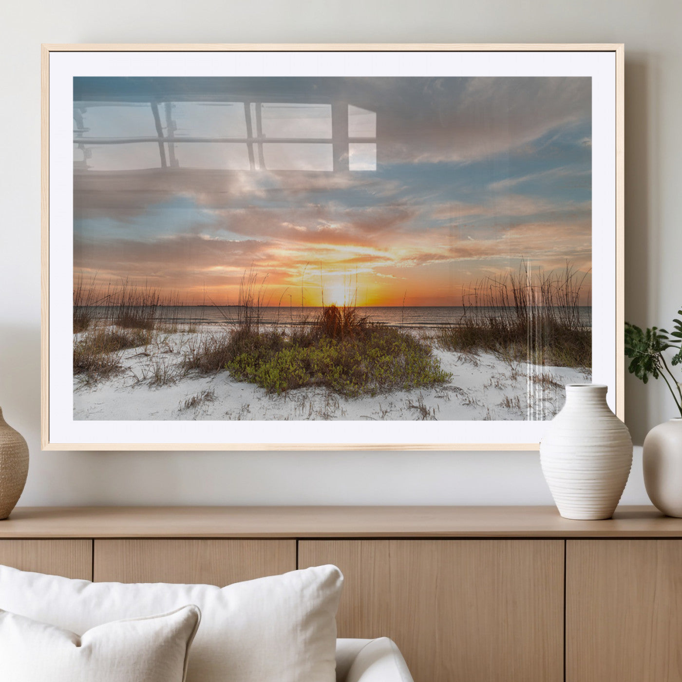A tranquil beach scene featuring golden sunset hues over the water, with grasses in the foreground and a peaceful, serene atmosphere.