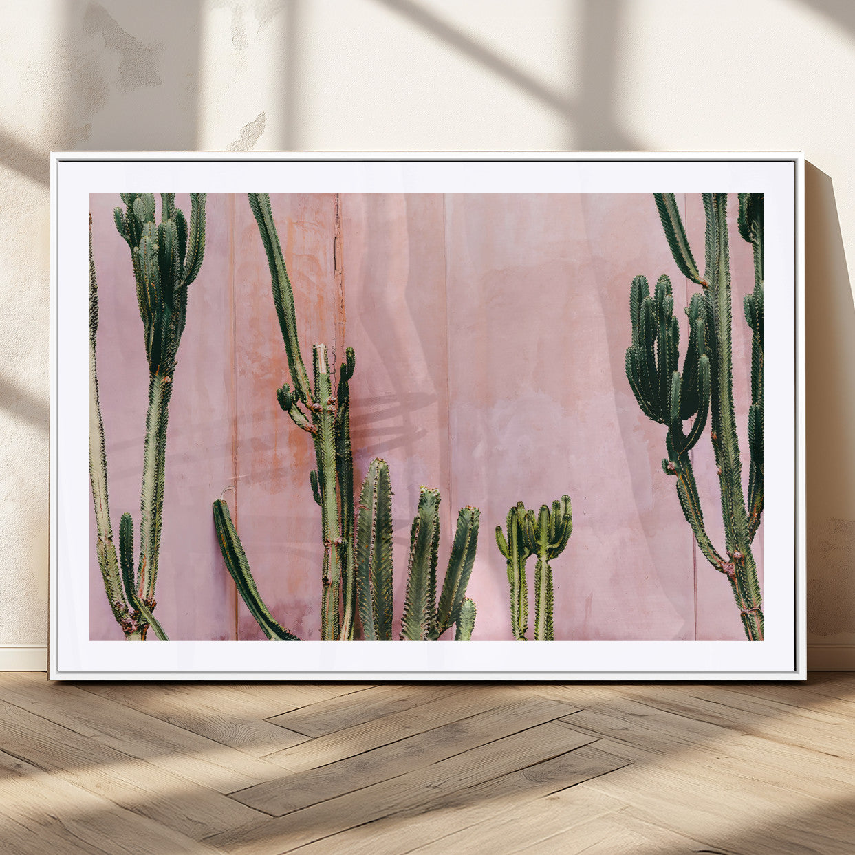 Framed canvas of tall green cacti against a soft pink wall, ideal for modern desert or colorful southwest-inspired home decor.