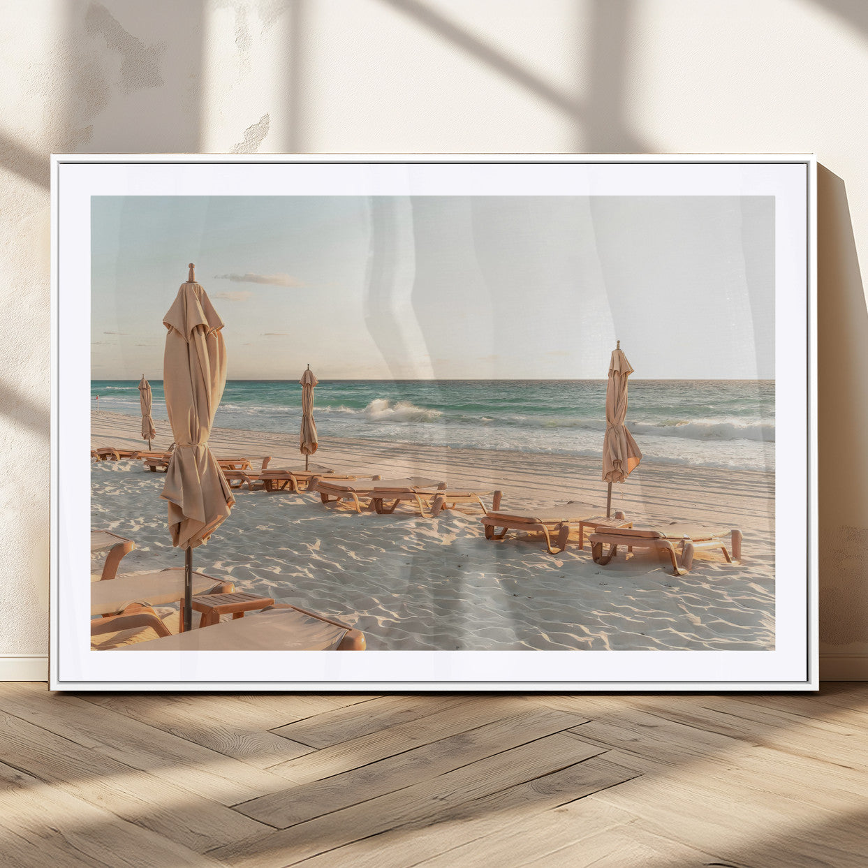 Minimalist photo of empty beach loungers and umbrellas on soft sand, ideal for calm seaside or pastel coastal-style home decor.