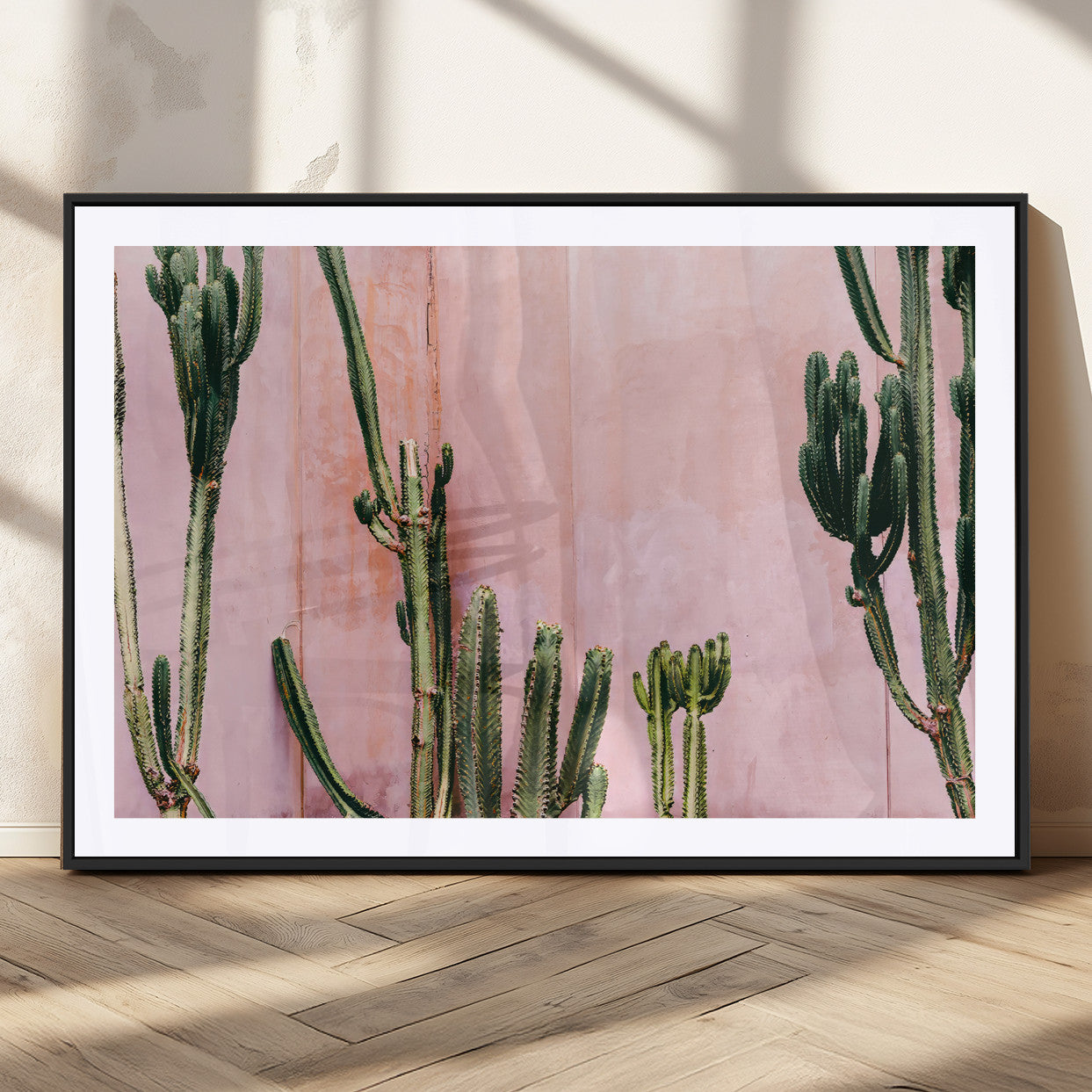 Framed canvas of tall green cacti against a soft pink wall, ideal for modern desert or colorful southwest-inspired home decor.