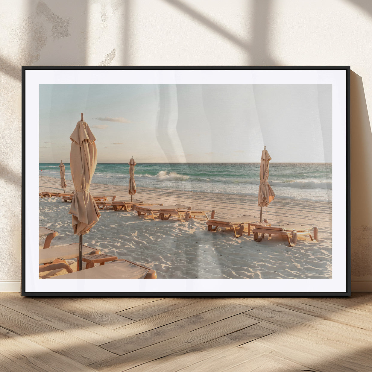 Minimalist photo of empty beach loungers and umbrellas on soft sand, ideal for calm seaside or pastel coastal-style home decor.