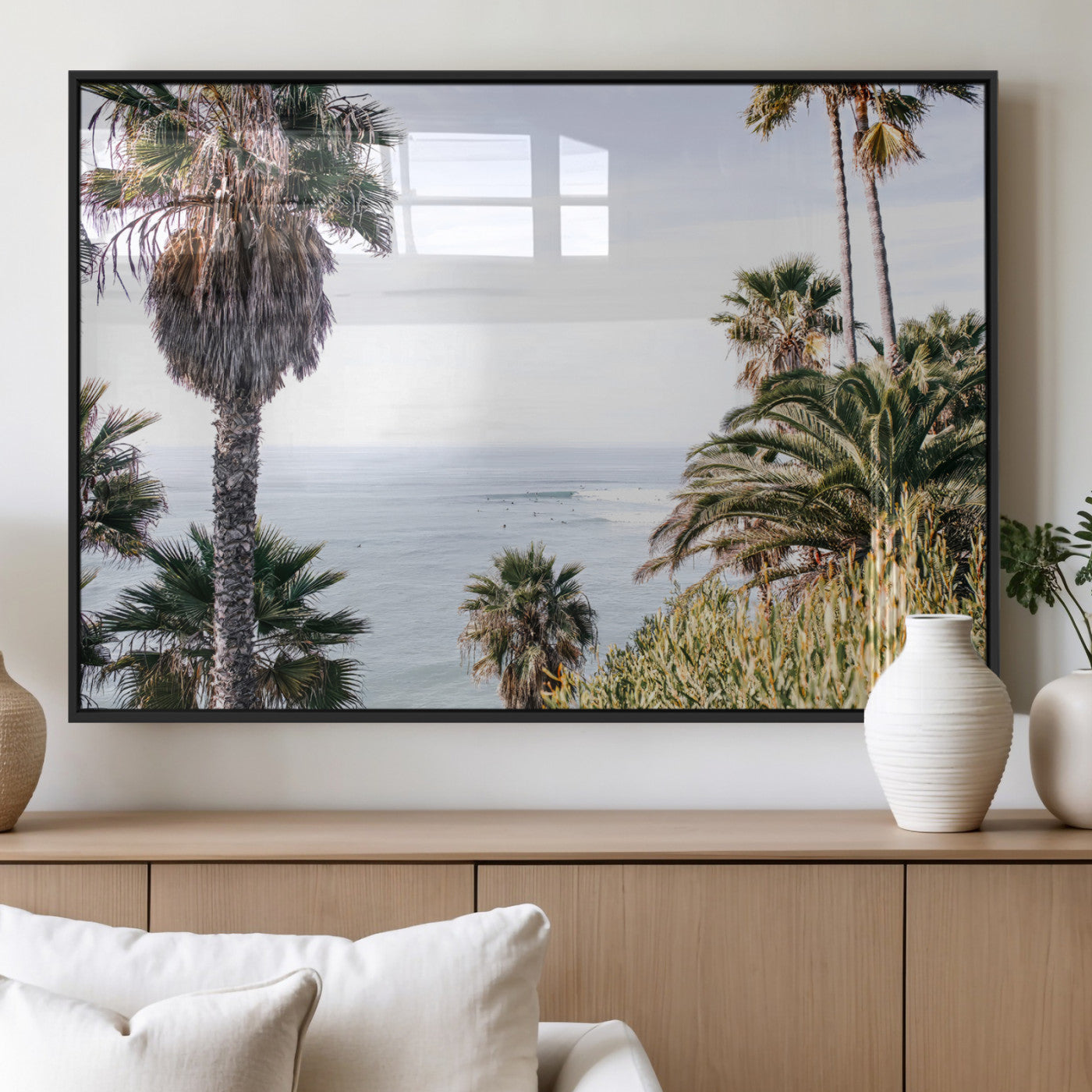 Scenic coastal view with tall palm trees overlooking a calm ocean, soft blue waves, and surfers in the distance, creating a peaceful tropical vibe.