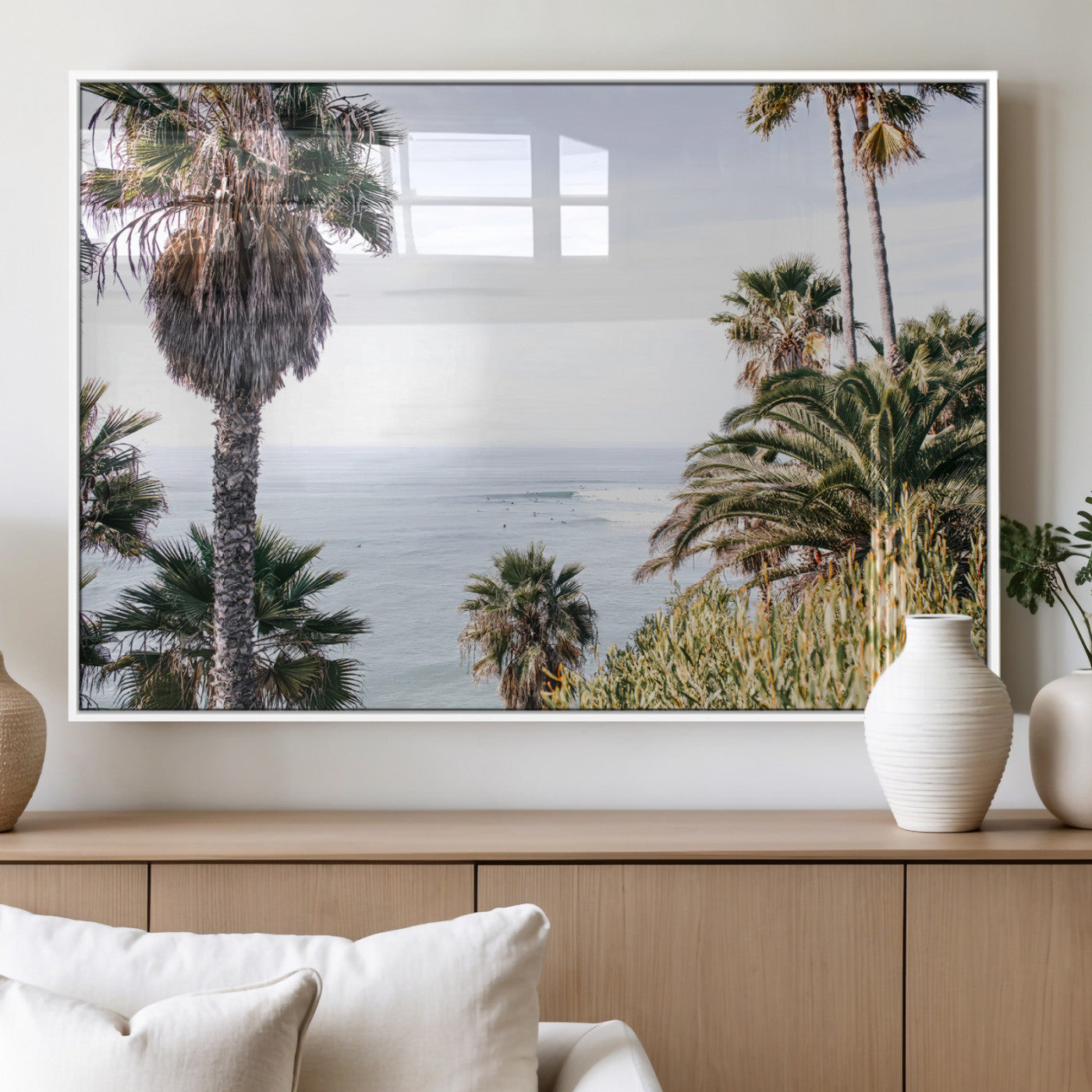 Scenic coastal view with tall palm trees overlooking a calm ocean, soft blue waves, and surfers in the distance, creating a peaceful tropical vibe.
