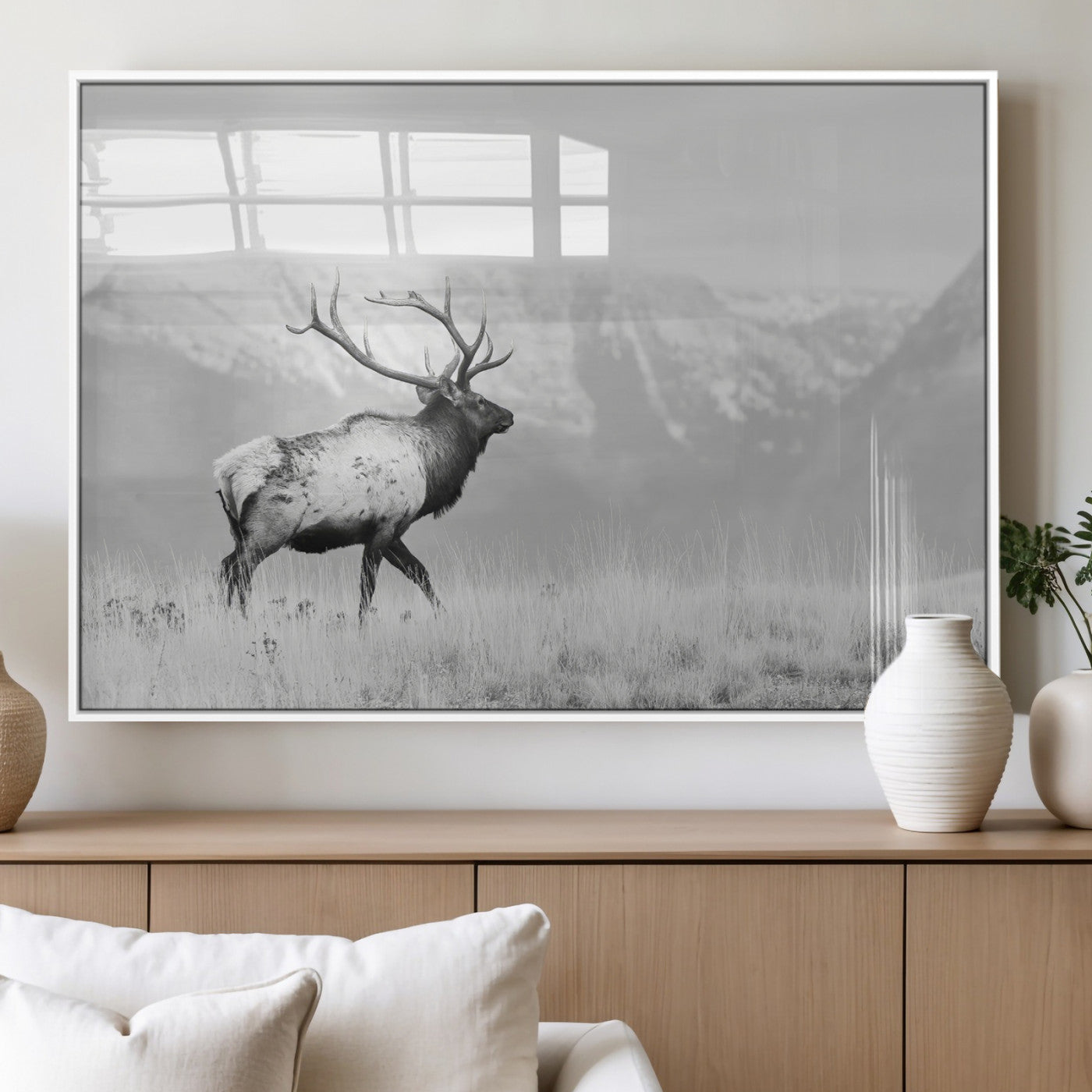 Black and white photograph of a majestic elk standing in a grassy field with snow-capped mountains in the background, creating a bold and rustic wilderness scene.
