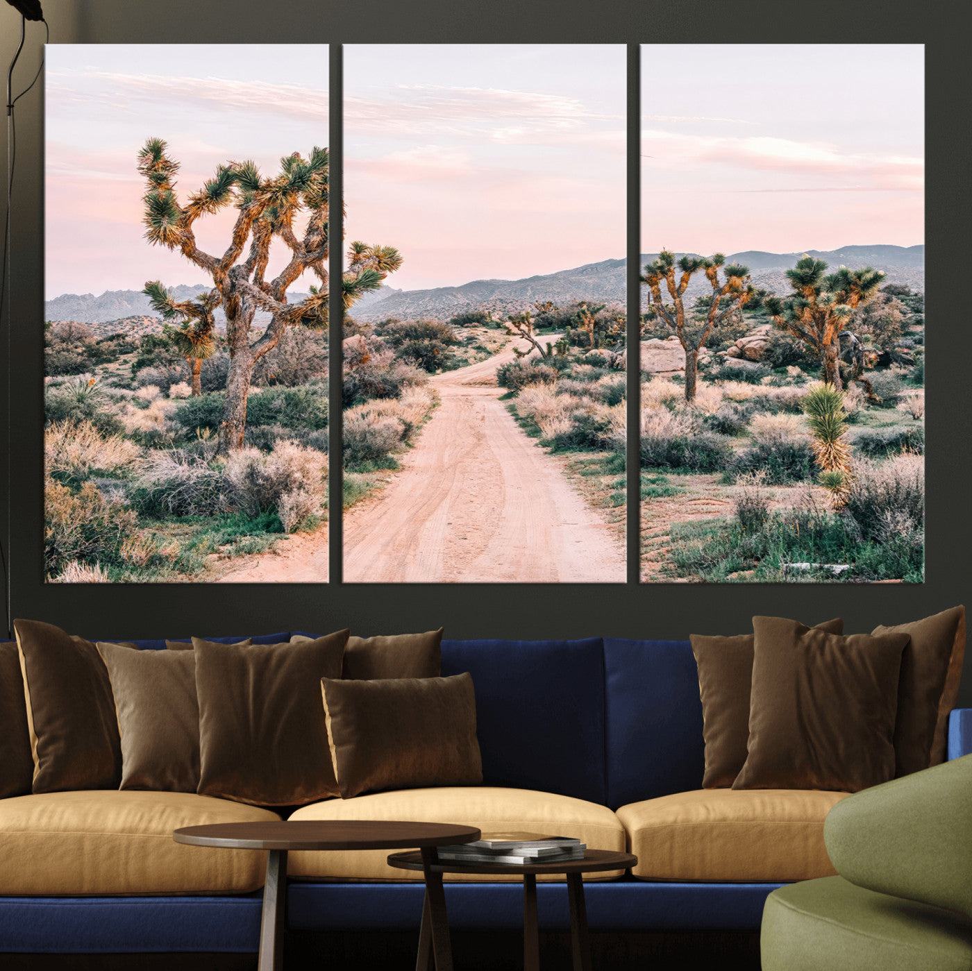 A dusty road winding through Joshua Tree National Park, framed by iconic twisted trees and warm desert tones under a soft pastel sky.