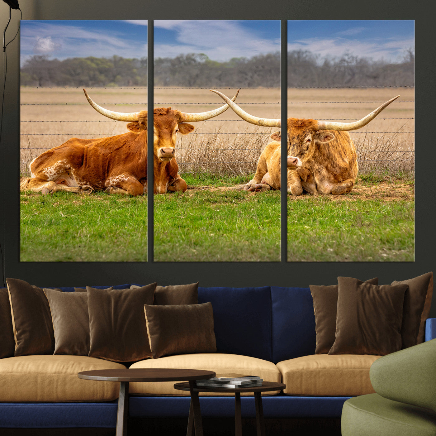 Two longhorn cows lying on green grass in front of a golden field and trees under a blue sky, perfect for rustic country wall decor.