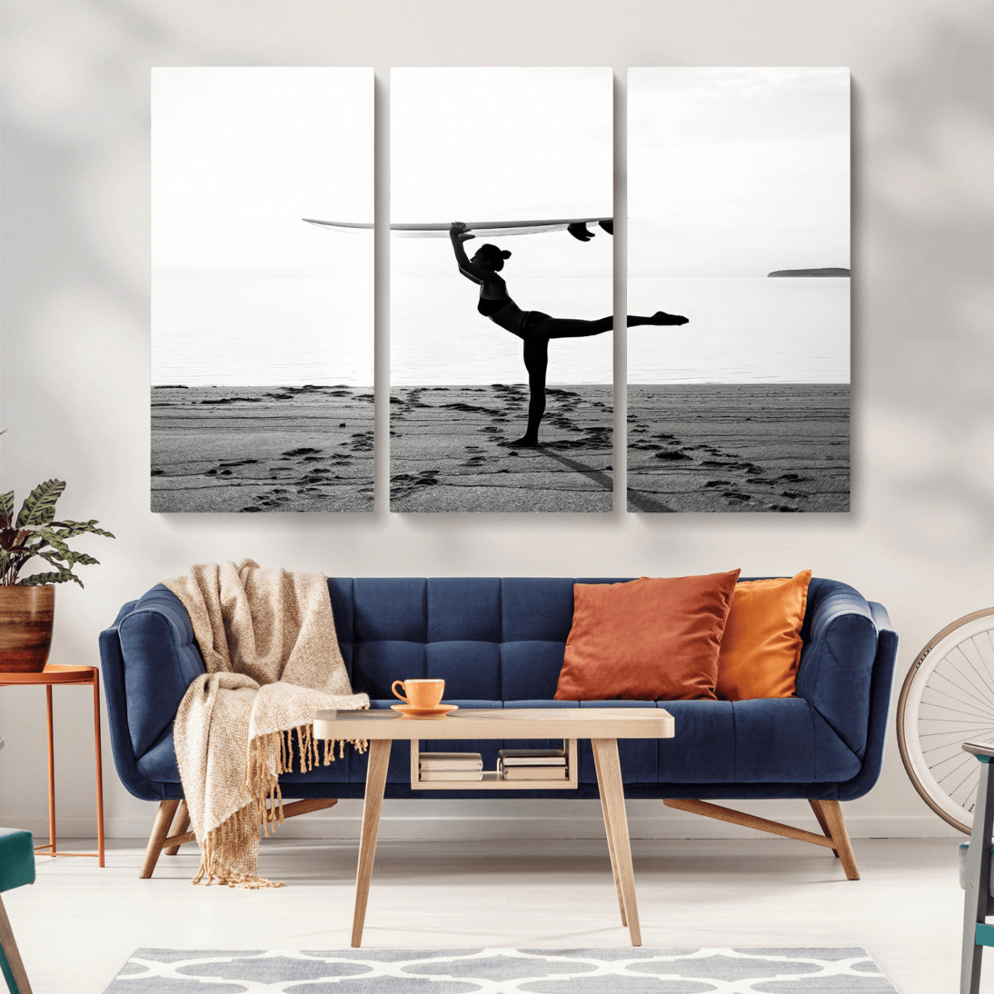 A woman balances a surfboard on her head while striking a yoga pose on the beach, silhouetted against a calm ocean horizon.