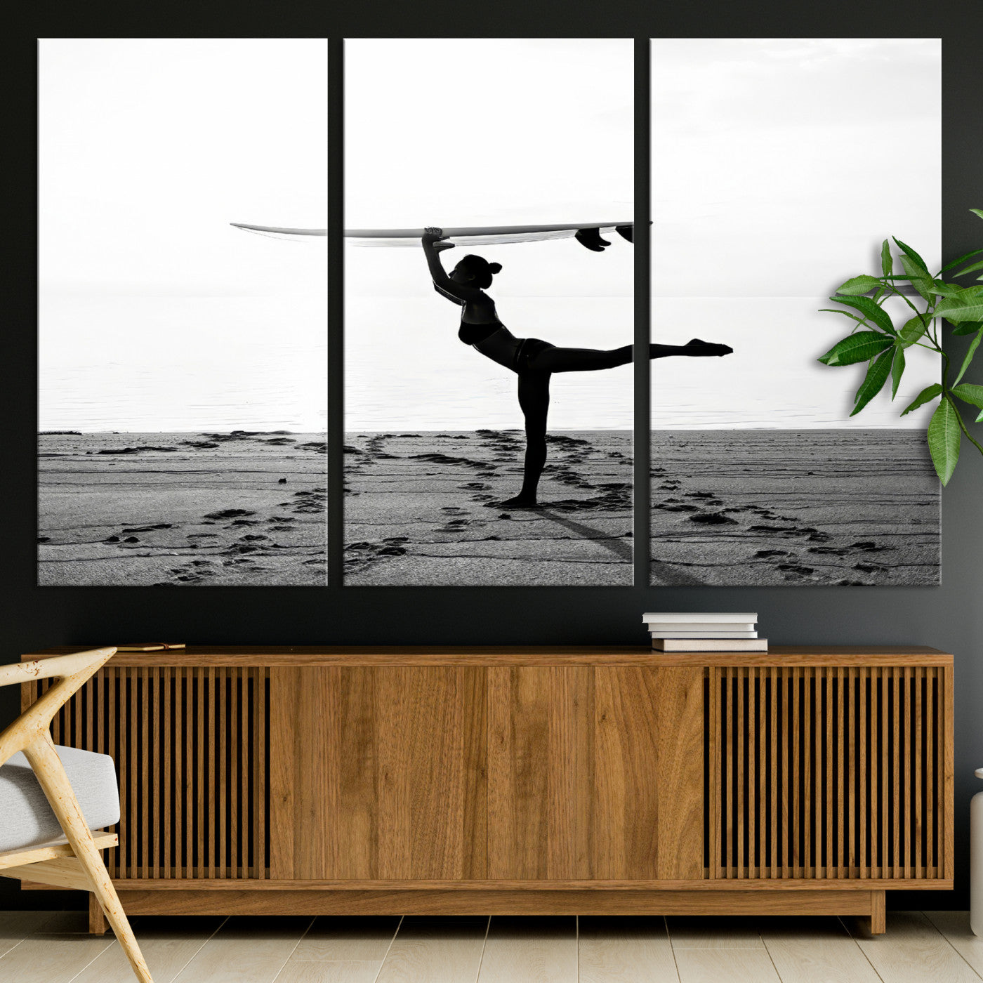 A woman balances a surfboard on her head while striking a yoga pose on the beach, silhouetted against a calm ocean horizon.