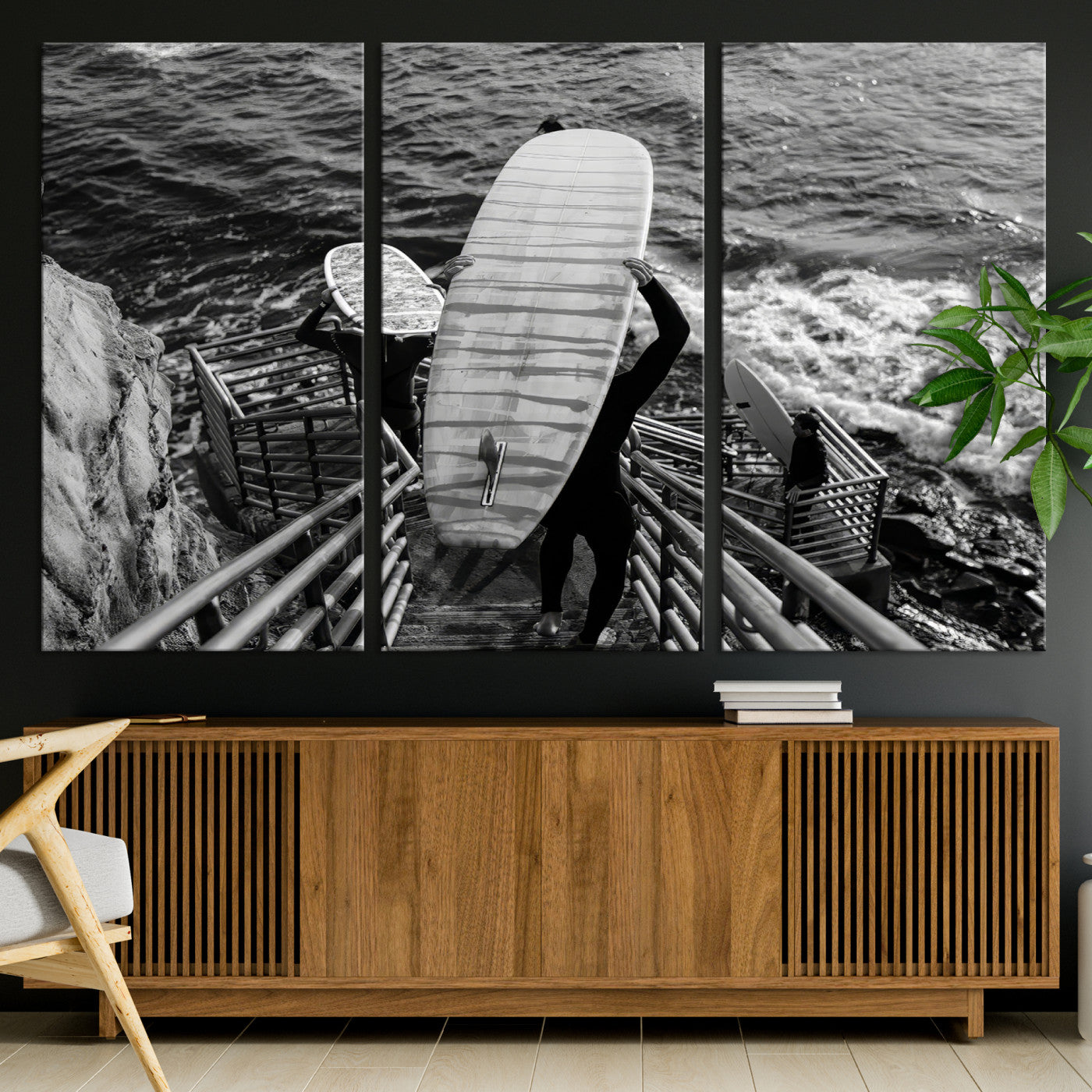 Black and white photo of surfers carrying boards down a rugged cliffside stairway, capturing a bold and adventurous coastal scene.