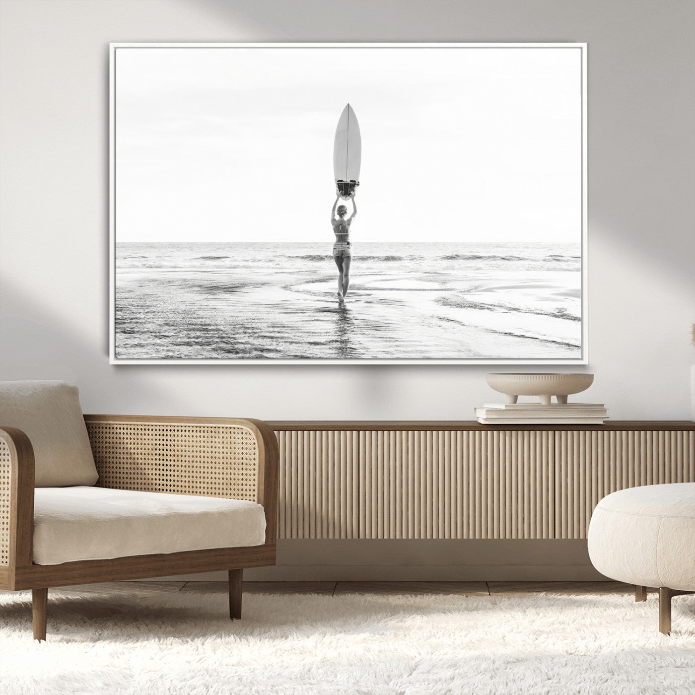 Black and white image of a female surfer holding a surfboard above her head while walking toward the ocean, creating a minimalist and bold coastal aesthetic.