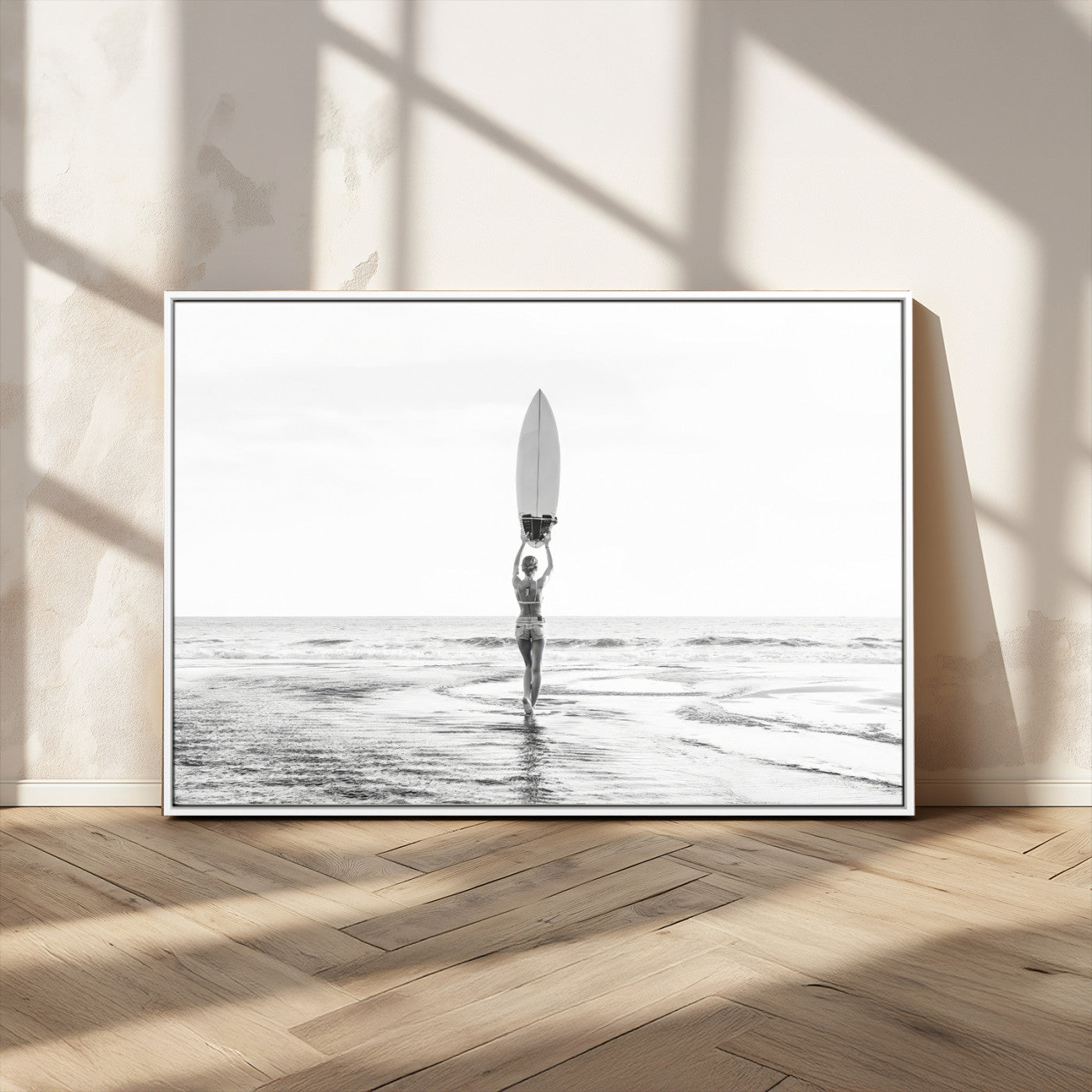 Black and white image of a female surfer holding a surfboard above her head while walking toward the ocean, creating a minimalist and bold coastal aesthetic.