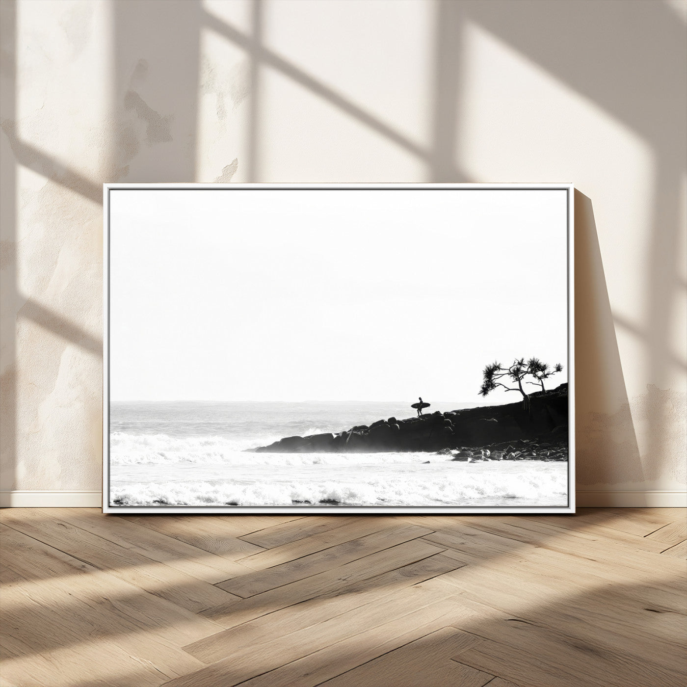 Black and white photo of a surfer standing on rocky cliffs, gazing at the waves, embodying the spirit of adventure and solitude.