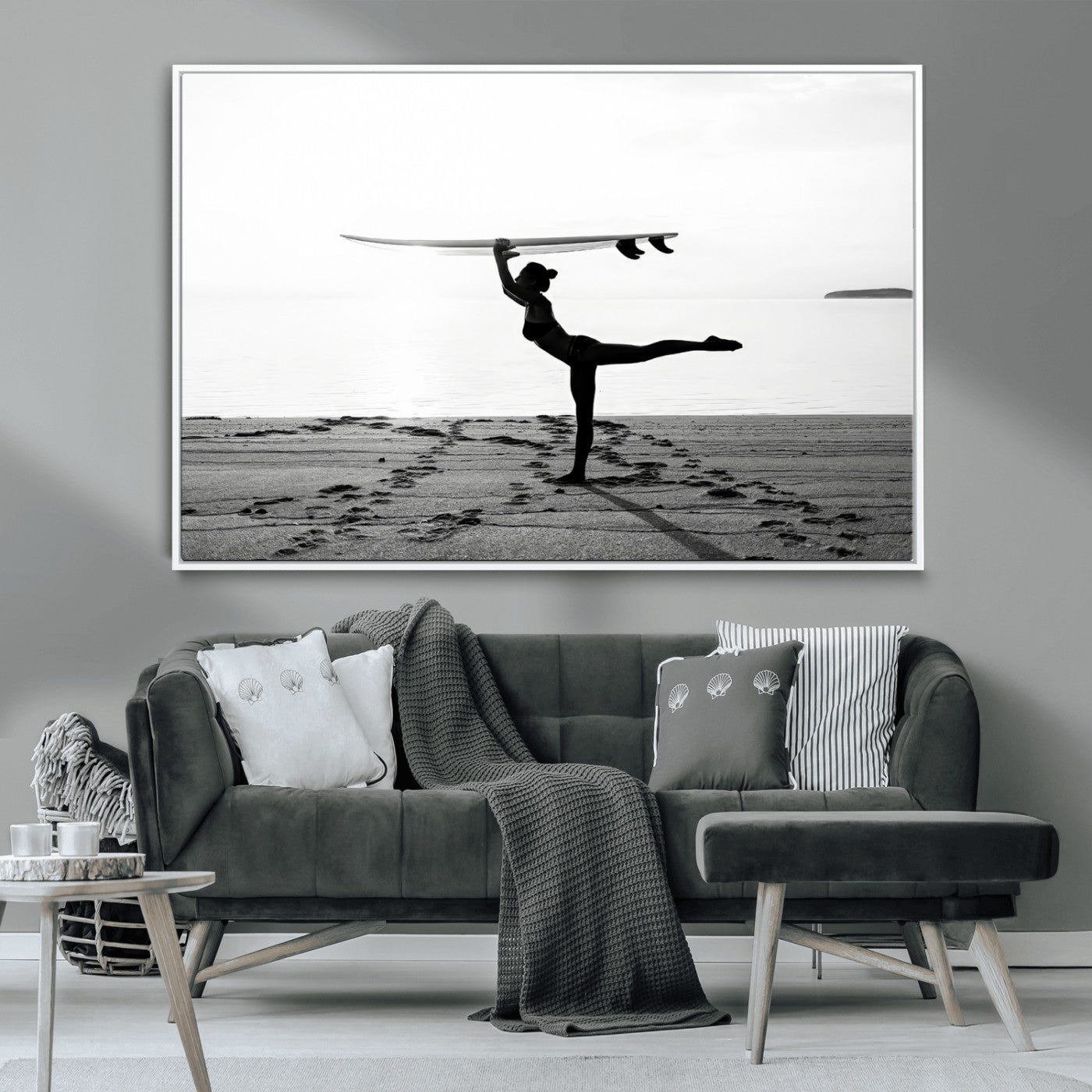 A woman balances a surfboard on her head while striking a yoga pose on the beach, silhouetted against a calm ocean horizon.