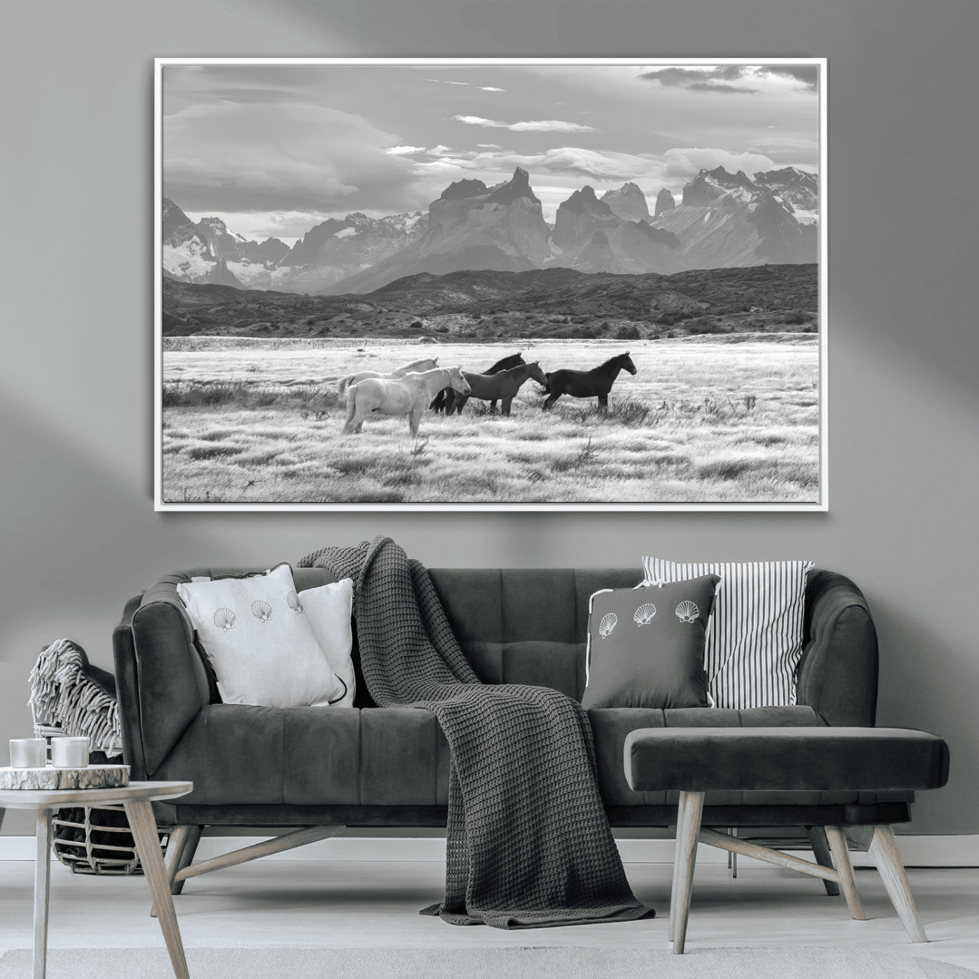 A black and white landscape of wild horses grazing in a vast grassland with towering mountains in the background, creating a moody and rustic western aesthetic.