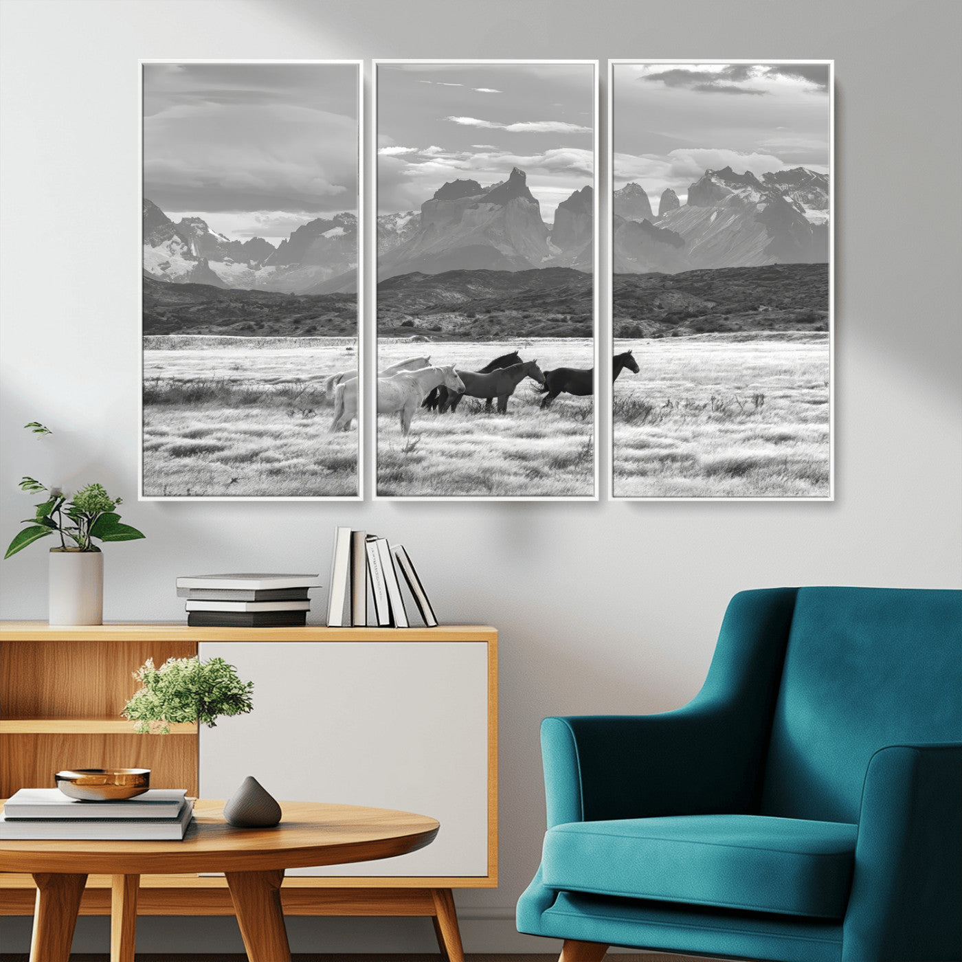 A black and white landscape of wild horses grazing in a vast grassland with towering mountains in the background, creating a moody and rustic western aesthetic.
