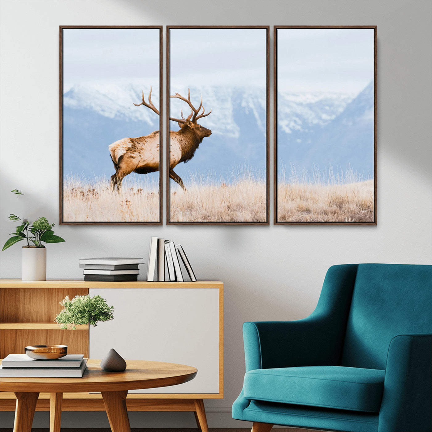 An elk walking on snowy grassland with majestic mountains in the background, ideal for rustic lodge or cabin wall decor.