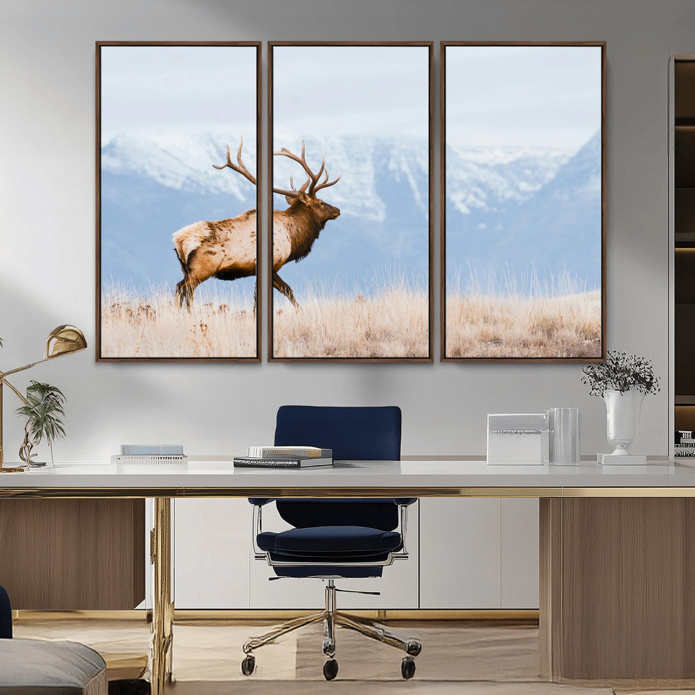 An elk walking on snowy grassland with majestic mountains in the background, ideal for rustic lodge or cabin wall decor.