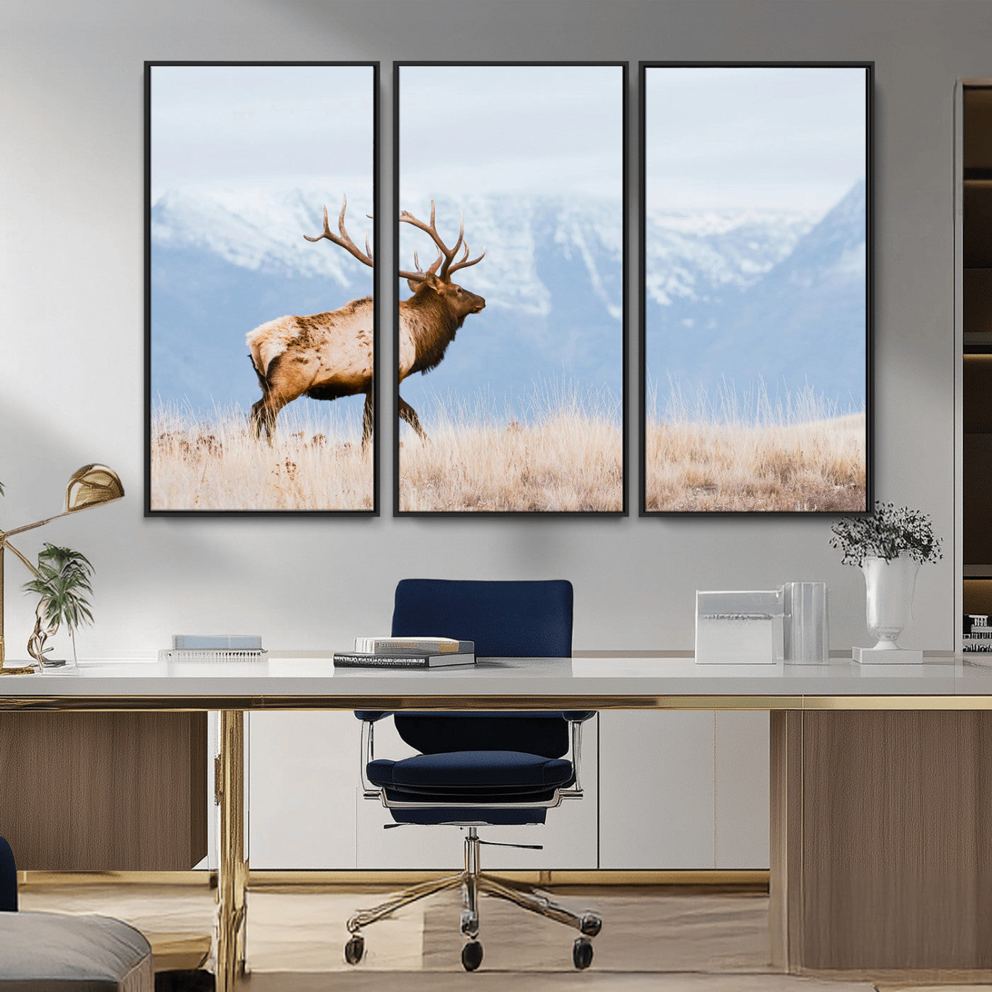 An elk walking on snowy grassland with majestic mountains in the background, ideal for rustic lodge or cabin wall decor.
