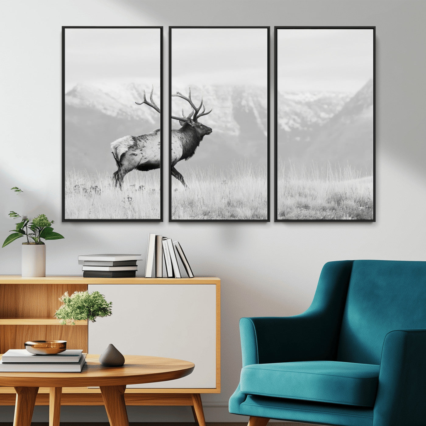 Black and white photograph of a majestic elk standing in a grassy field with snow-capped mountains in the background, creating a bold and rustic wilderness scene.