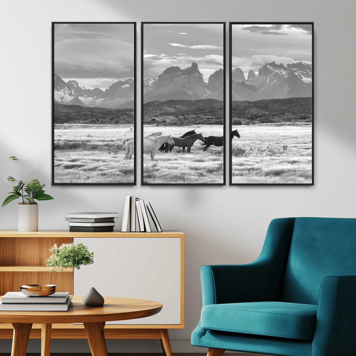 A black and white landscape of wild horses grazing in a vast grassland with towering mountains in the background, creating a moody and rustic western aesthetic.