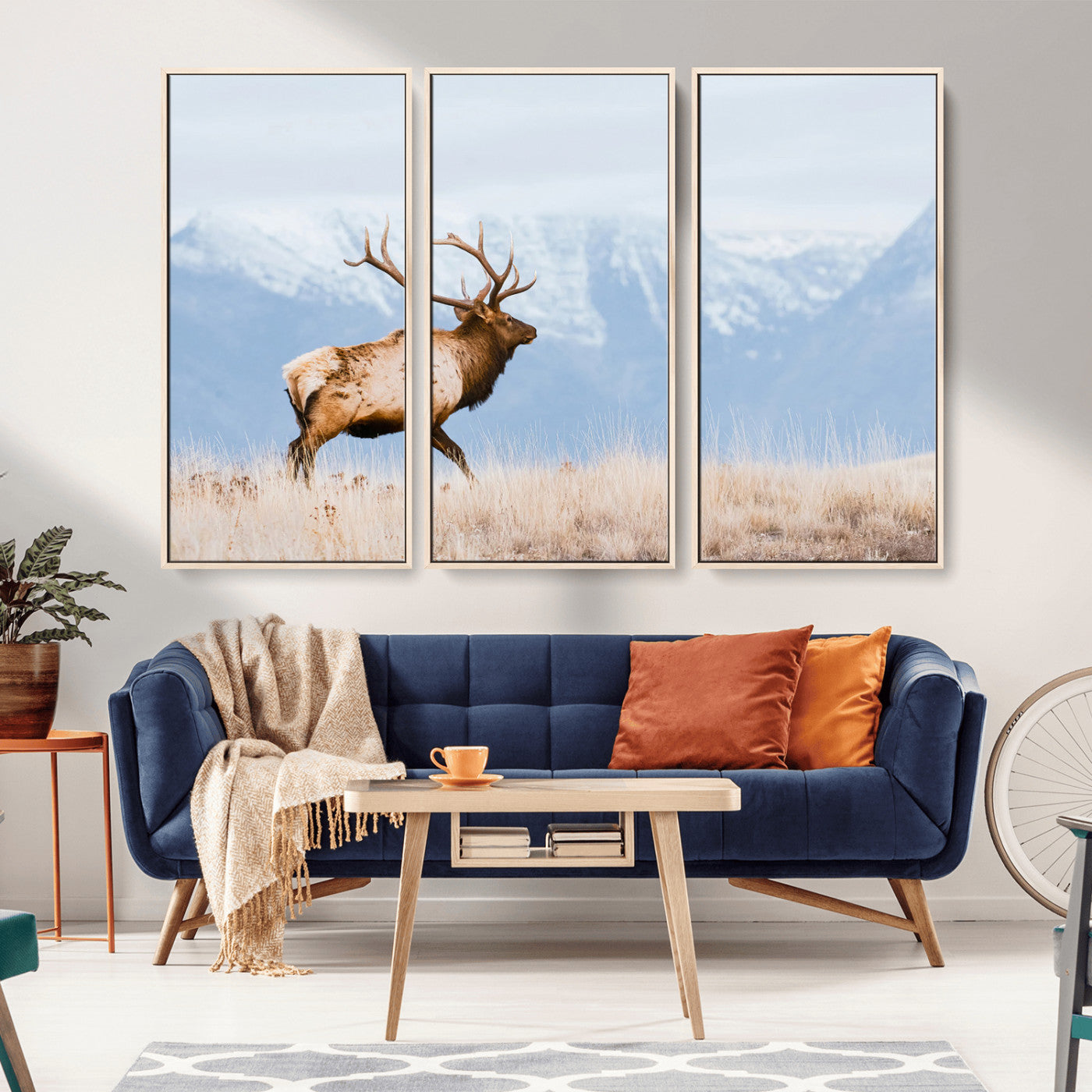 An elk walking on snowy grassland with majestic mountains in the background, ideal for rustic lodge or cabin wall decor.