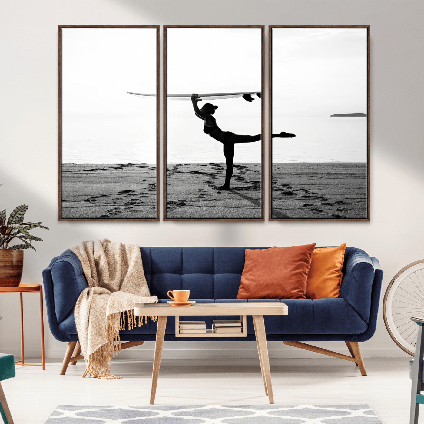A woman balances a surfboard on her head while striking a yoga pose on the beach, silhouetted against a calm ocean horizon.