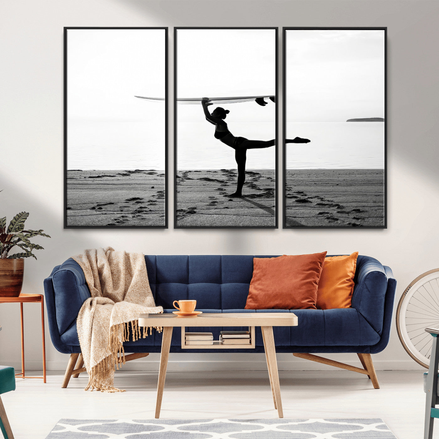 A woman balances a surfboard on her head while striking a yoga pose on the beach, silhouetted against a calm ocean horizon.