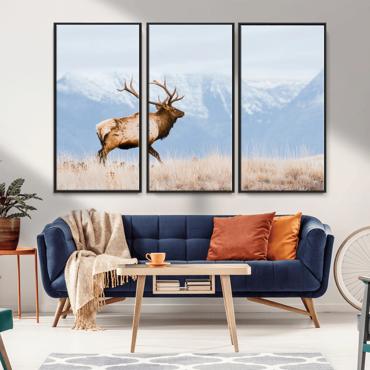 An elk walking on snowy grassland with majestic mountains in the background, ideal for rustic lodge or cabin wall decor.