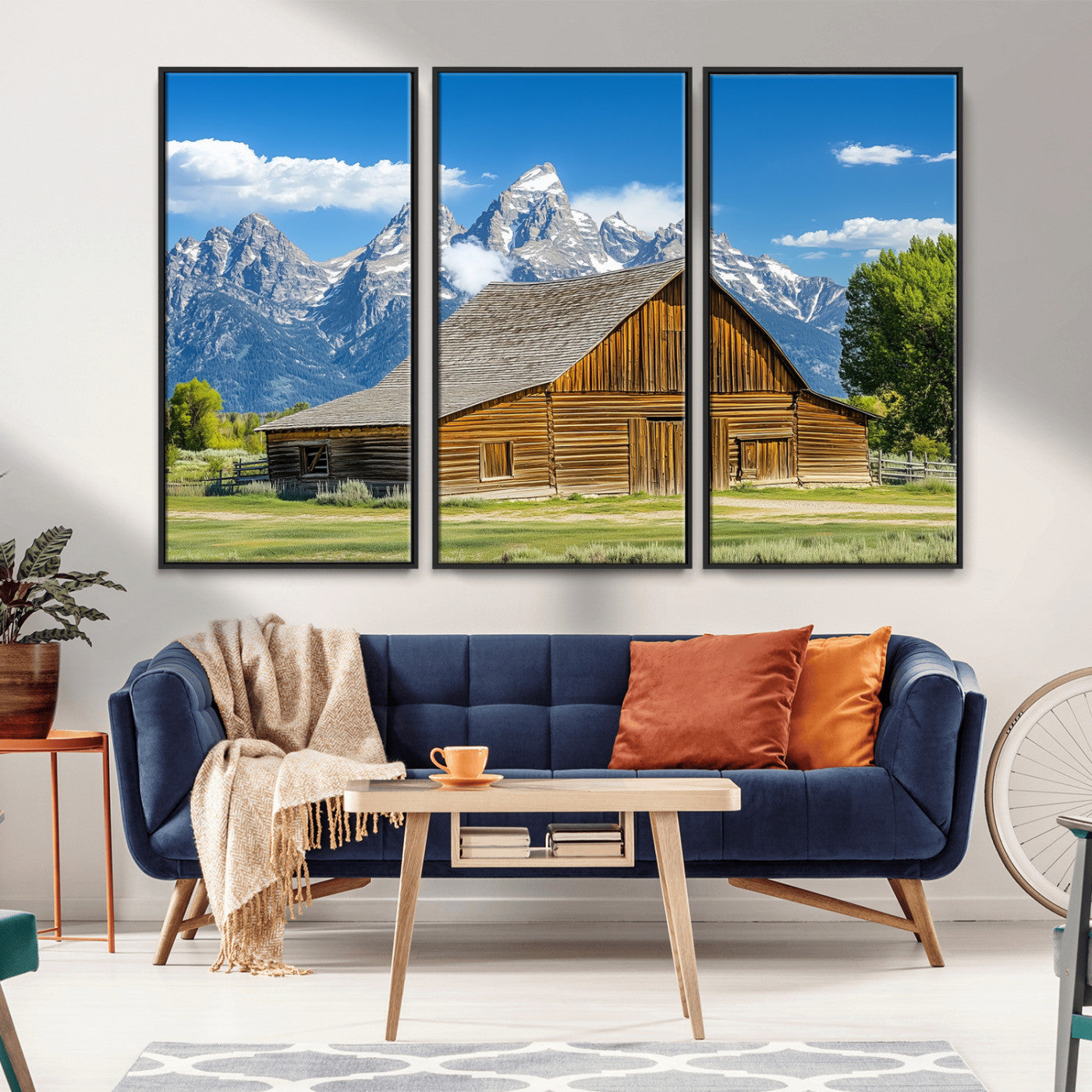 A rustic wooden barn sits in front of towering mountain peaks under a clear blue sky, perfect for farmhouse or cabin style interiors.