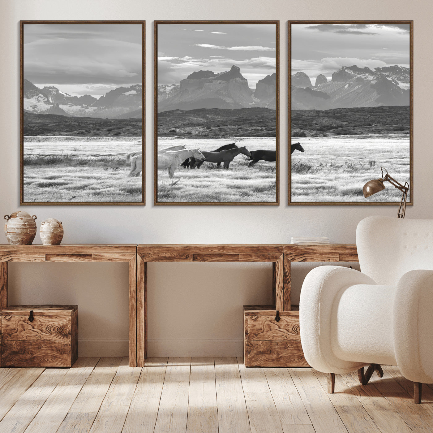 A black and white landscape of wild horses grazing in a vast grassland with towering mountains in the background, creating a moody and rustic western aesthetic.