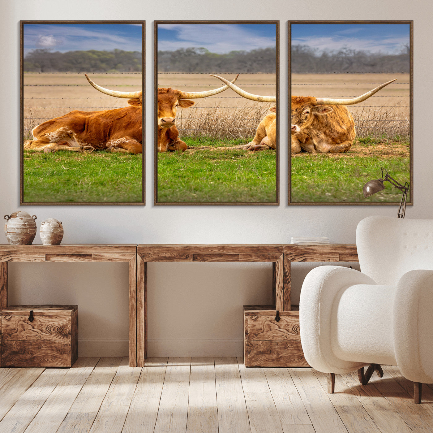 Two longhorn cows lying on green grass in front of a golden field and trees under a blue sky, perfect for rustic country wall decor.