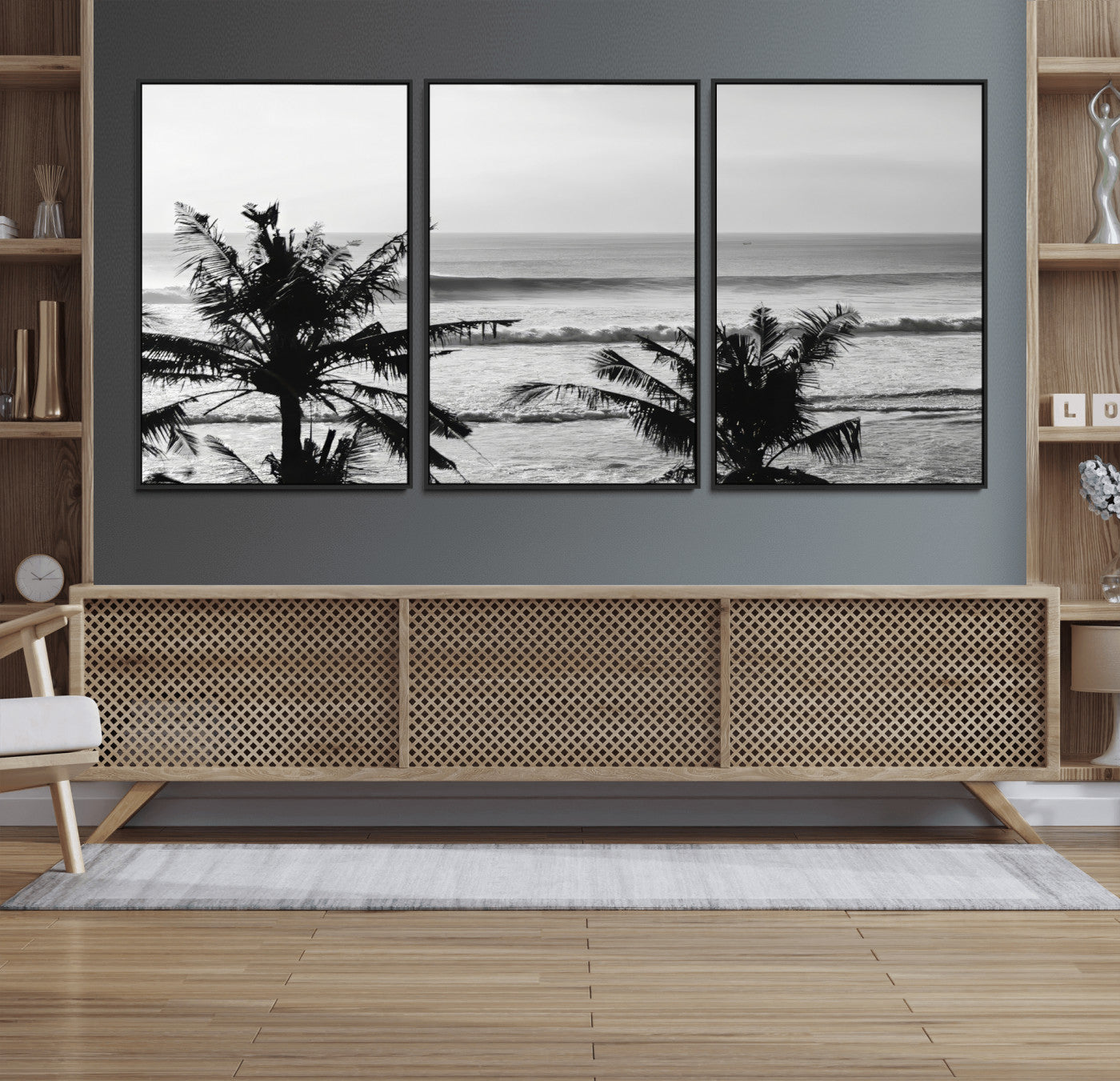 Black and white view of ocean waves crashing on a tropical coastline, framed by silhouetted palm trees under a vast, open sky.