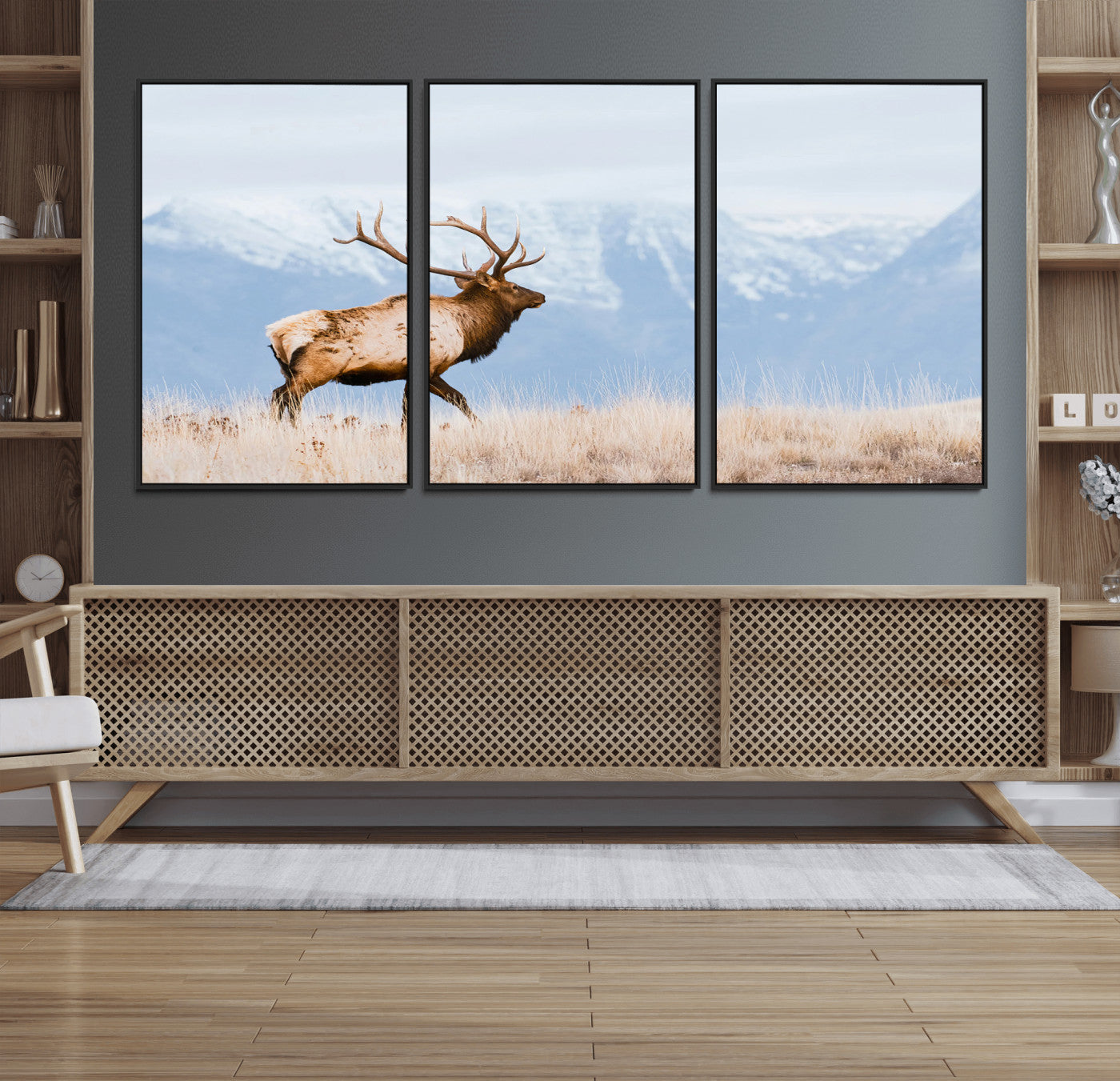 An elk walking on snowy grassland with majestic mountains in the background, ideal for rustic lodge or cabin wall decor.