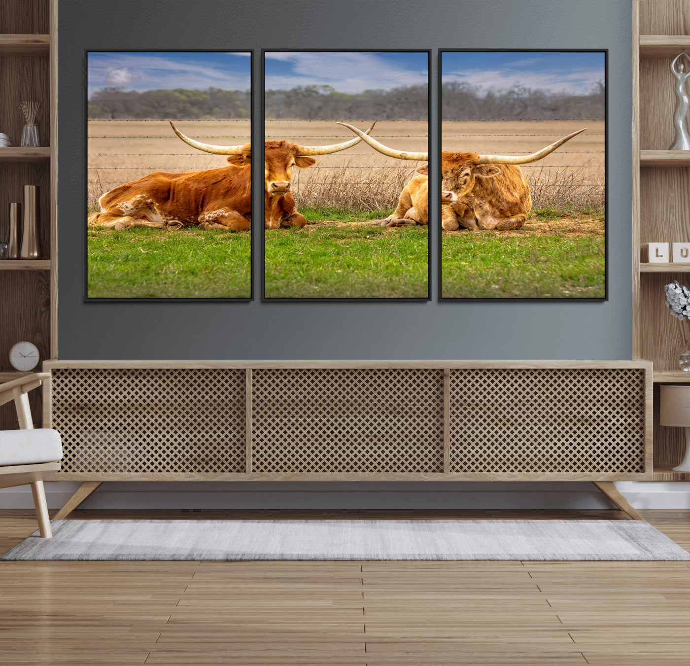 Two longhorn cows lying on green grass in front of a golden field and trees under a blue sky, perfect for rustic country wall decor.