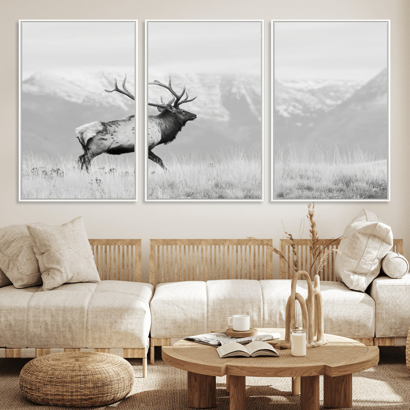Black and white photograph of a majestic elk standing in a grassy field with snow-capped mountains in the background, creating a bold and rustic wilderness scene.