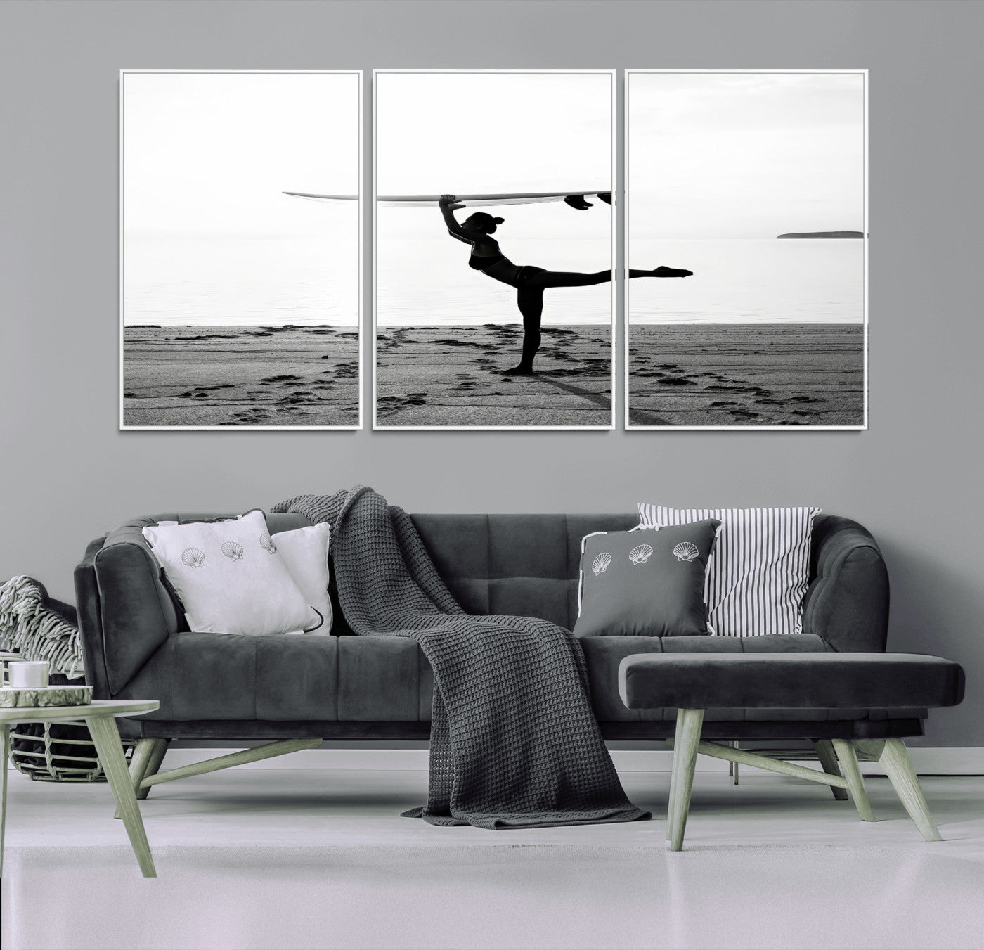 A woman balances a surfboard on her head while striking a yoga pose on the beach, silhouetted against a calm ocean horizon.