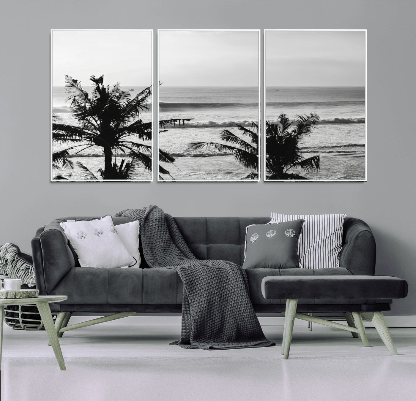 Black and white view of ocean waves crashing on a tropical coastline, framed by silhouetted palm trees under a vast, open sky.