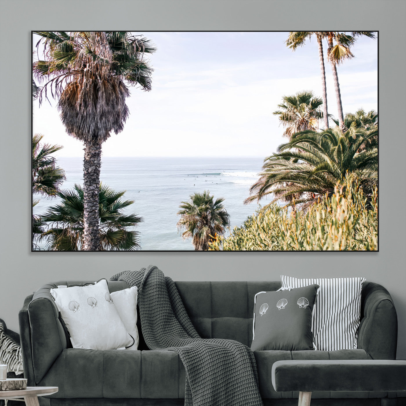 Scenic coastal view with tall palm trees overlooking a calm ocean, soft blue waves, and surfers in the distance, creating a peaceful tropical vibe.