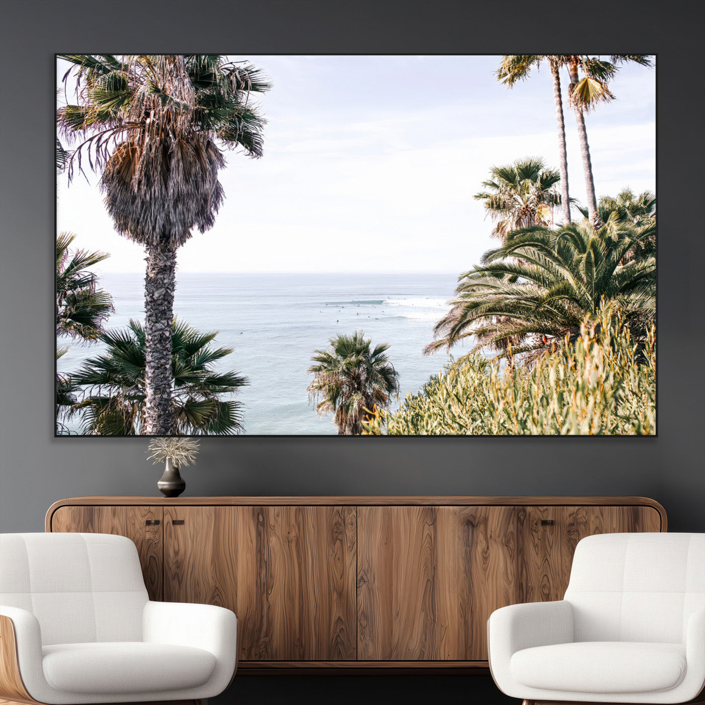 Scenic coastal view with tall palm trees overlooking a calm ocean, soft blue waves, and surfers in the distance, creating a peaceful tropical vibe.