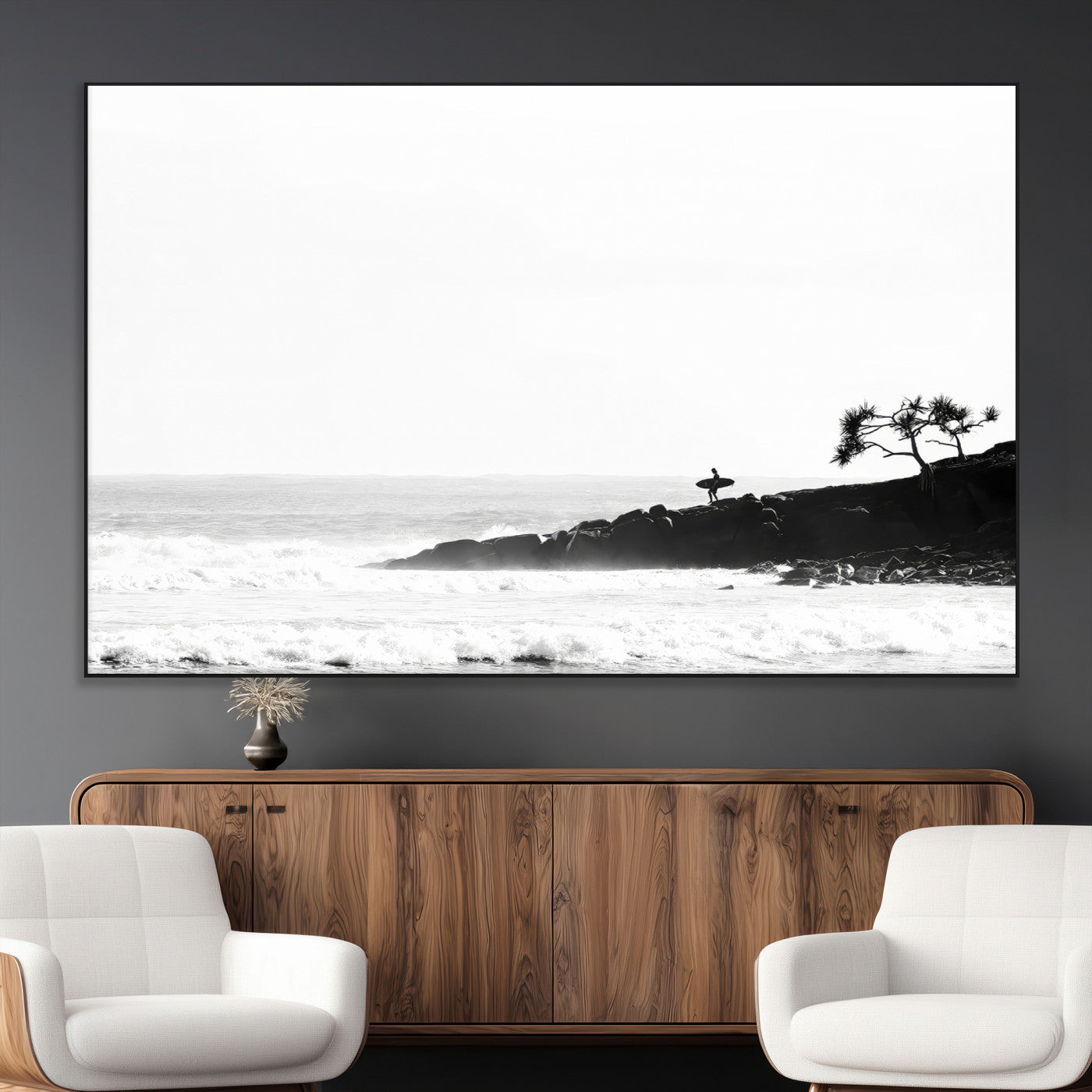 Black and white photo of a surfer standing on rocky cliffs, gazing at the waves, embodying the spirit of adventure and solitude.
