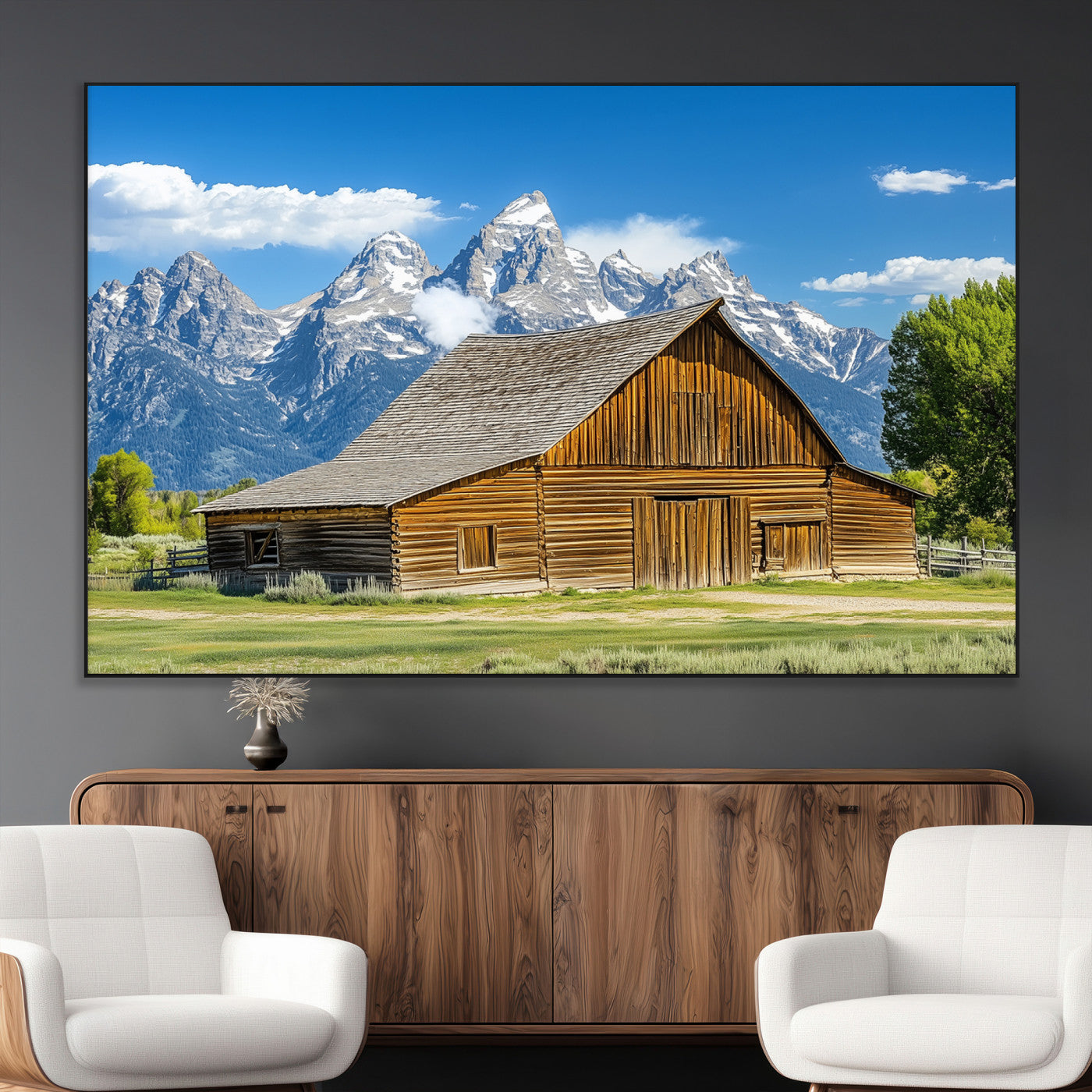 A rustic wooden barn sits in front of towering mountain peaks under a clear blue sky, perfect for farmhouse or cabin style interiors.