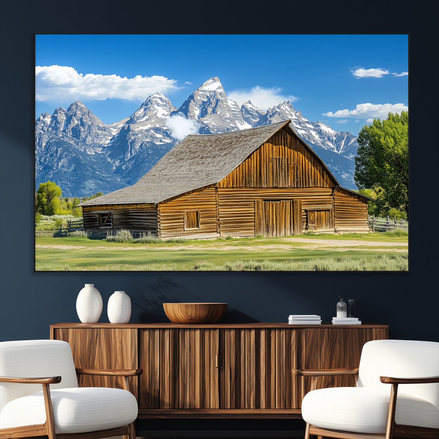 A rustic wooden barn sits in front of towering mountain peaks under a clear blue sky, perfect for farmhouse or cabin style interiors.