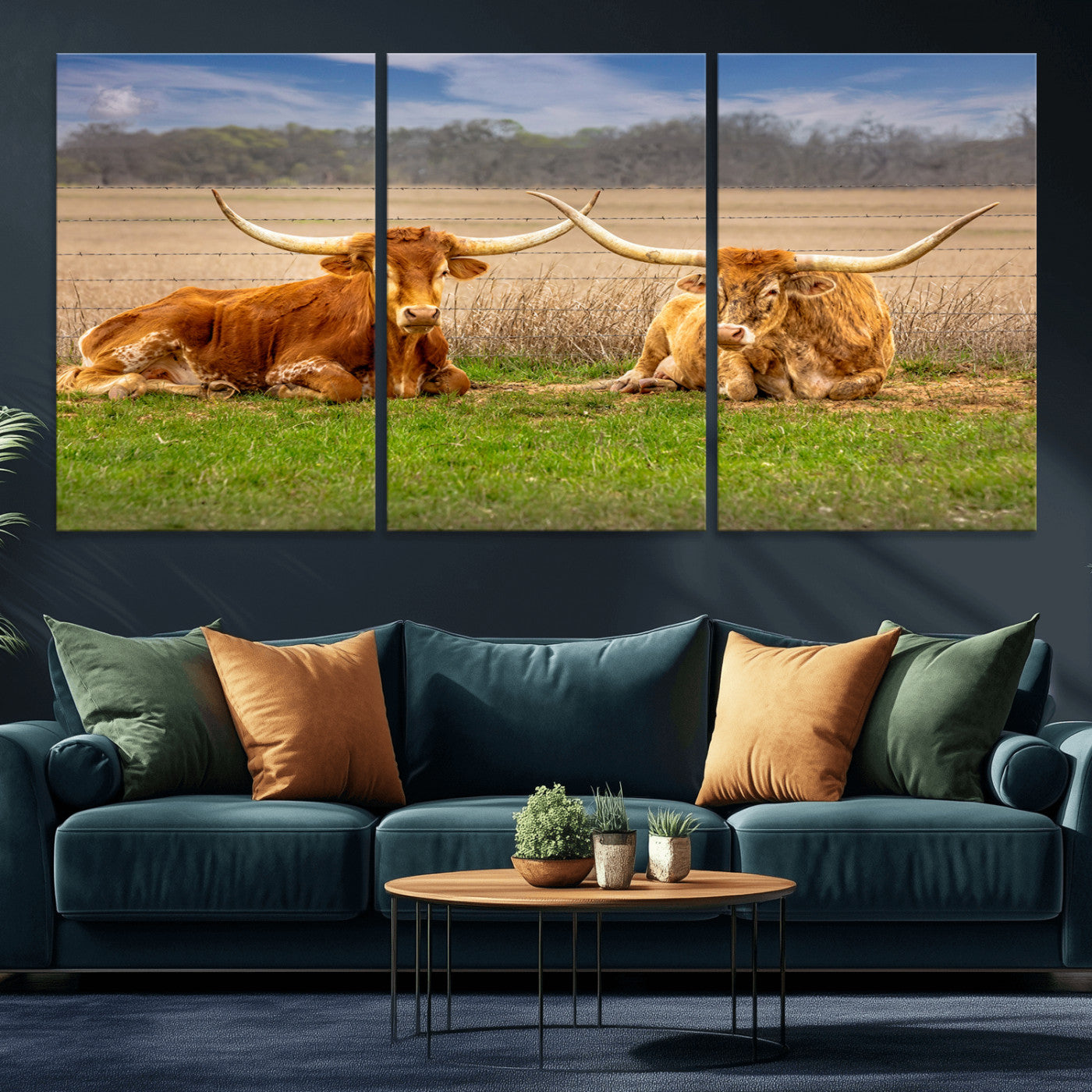 Two longhorn cows lying on green grass in front of a golden field and trees under a blue sky, perfect for rustic country wall decor.
