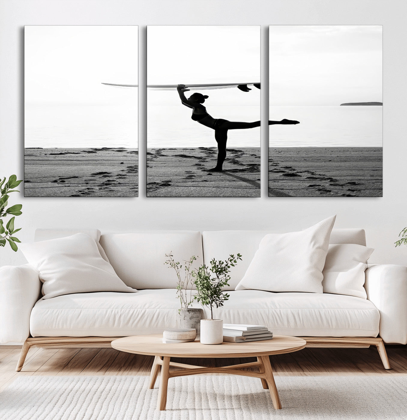 A woman balances a surfboard on her head while striking a yoga pose on the beach, silhouetted against a calm ocean horizon.