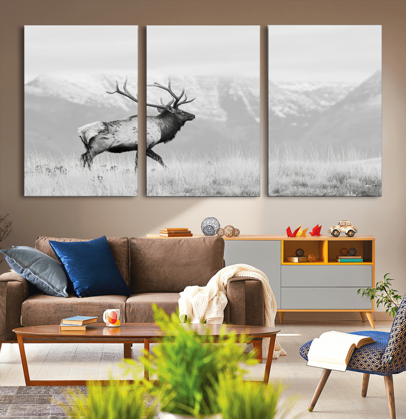 Black and white photograph of a majestic elk standing in a grassy field with snow-capped mountains in the background, creating a bold and rustic wilderness scene.