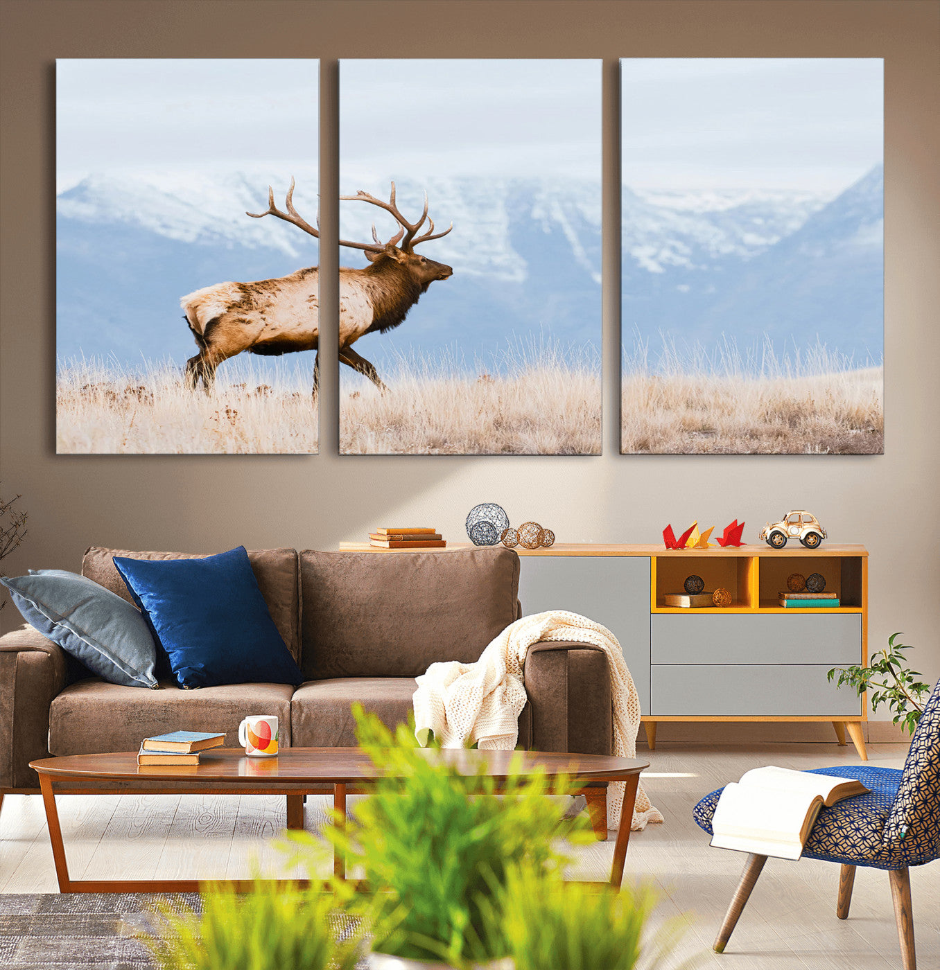 An elk walking on snowy grassland with majestic mountains in the background, ideal for rustic lodge or cabin wall decor.