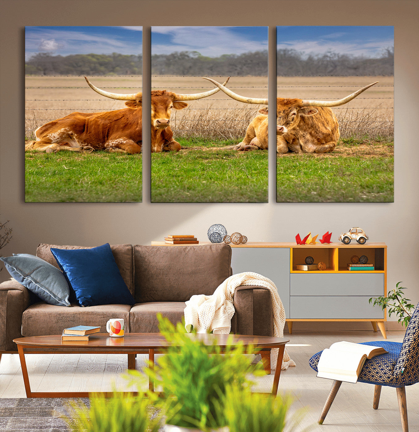Two longhorn cows lying on green grass in front of a golden field and trees under a blue sky, perfect for rustic country wall decor.